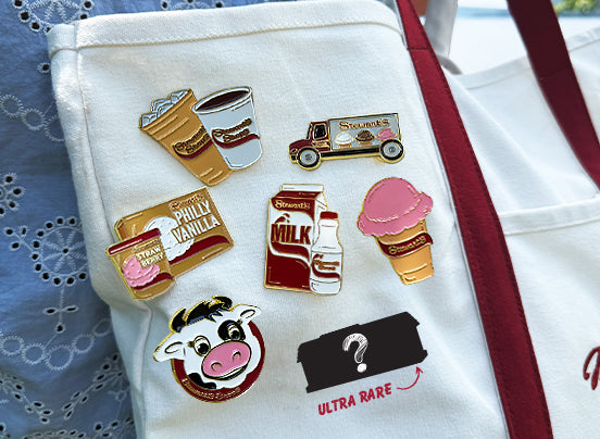 Canvas tote bag displaying Stewart's Shops collectible enamel pins featuring coffee, ice cream, milk, ice cream cartons, a delivery truck, a cow, and an ultra-rare mystery pin.