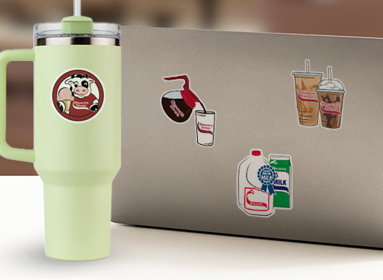 Light green tumbler with a straw next to a laptop with coffee-themed stickers.