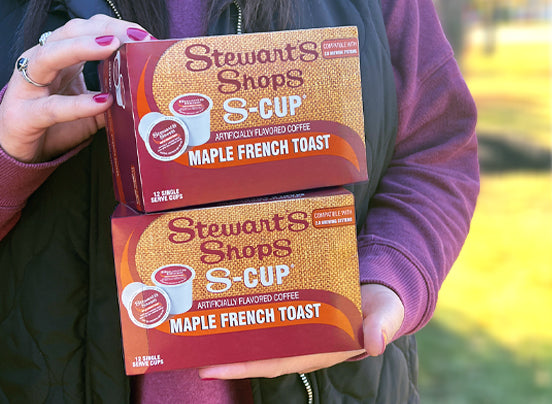 A person holding two boxes of Stewart's Shops Maple French Toast S-Cups while standing outside.