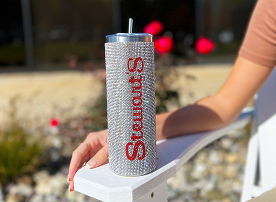 A bejeweled tumbler that says Stewarts down the side and a metal straw on chair