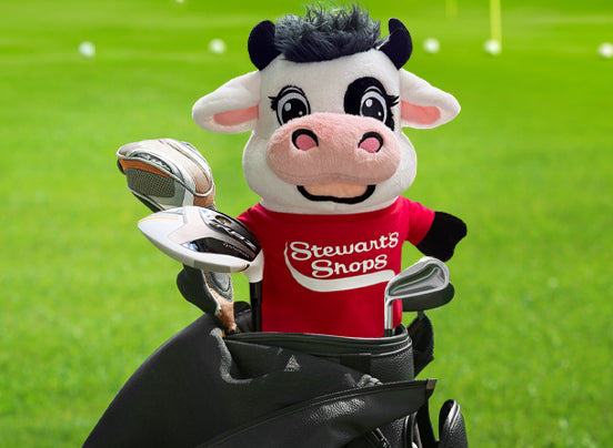 Cow mascot with golf club cover in a Stewart's Shops branded shirt on a green field