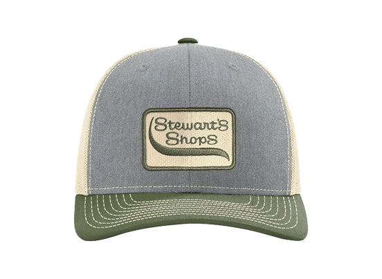 Front view of a Stewart's Shops trucker hat with a heather gray front panel, olive green curved bill, cream mesh sides and back, and an embroidered Stewart's Shops logo patch centered on the front.