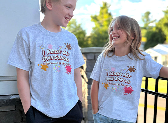 Two children wearing gray t-shirts with a printed design outdoors.