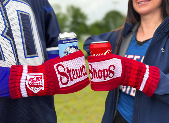 Two people wearing knit mitten can holders dressed in sports team gear holding beverages. 