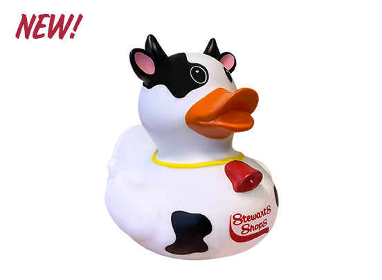 A novelty rubber duck designed to look like a cow. The duck has black and white cow-like markings, small black horns, and pink inner ears. It features a bright orange bill and a red Stewart’s Shops logo on its side. A red cowbell hangs from a yellow collar around its neck. The word “NEW!” appears in bold red text in the top left corner.
