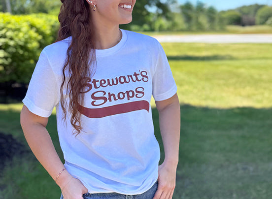 Person wearing a white t-shirt with 'Stewart's Shops' text outdoors.
