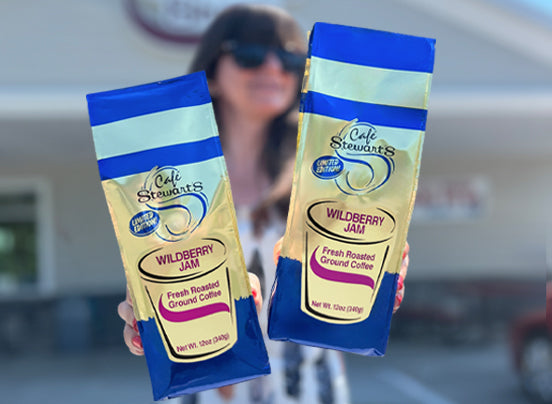 Two packages of Caffe Stewart's Wildberry Jam held by a person in front of a blurred background.