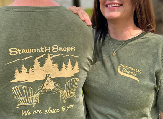 Stewarts Shops, We are closer to you green t-shirt with an Adirondack scene.  Woman wearing shirt, stewarts shops logo on front. 