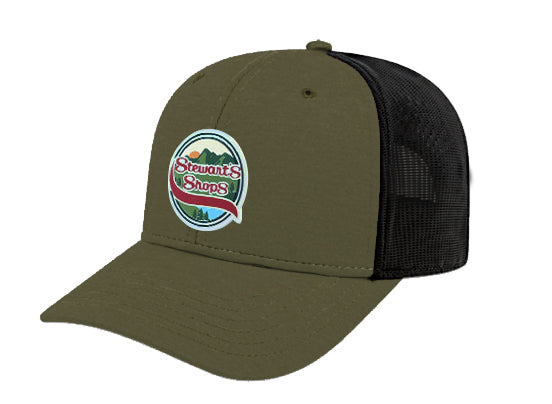 Olive green Stewart’s Shops trucker-style hat with a black mesh back. The front features a round patch design showing mountains, a sunset, and pine trees with the Stewart’s Shops logo in red and white. 