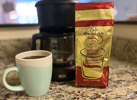 A coffee maker, mug filled with coffee and a 12 oz bag of ground house blend coffee